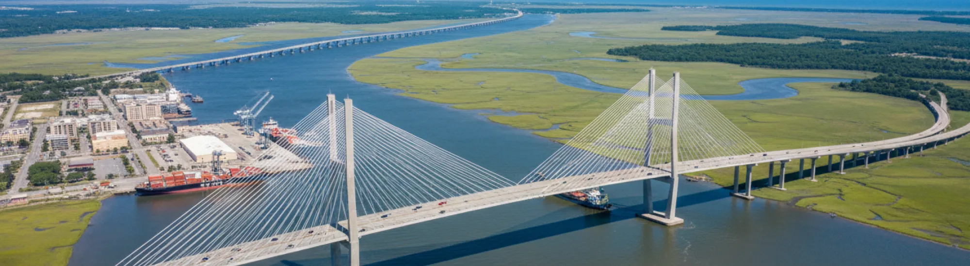 Suspension bridge over a wide river, surrounded by green fields.