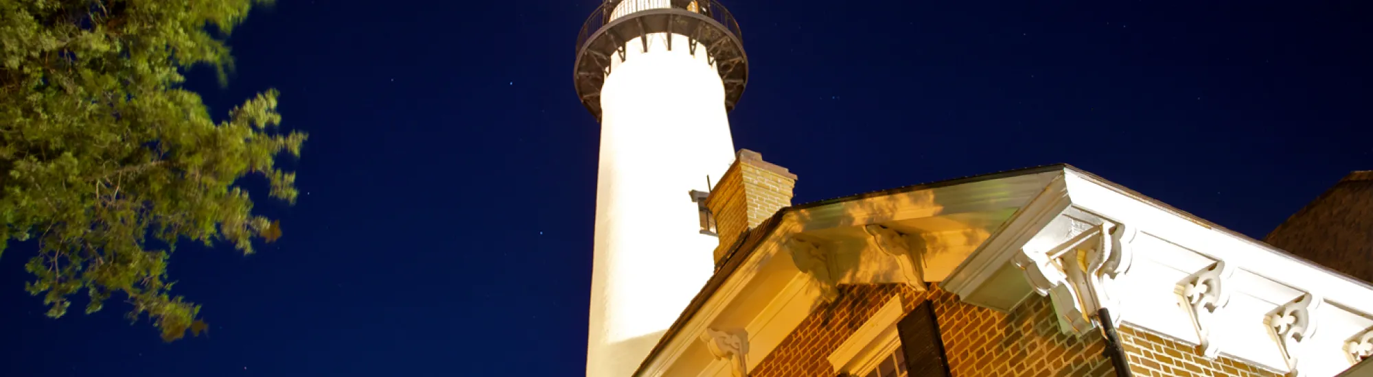 Lighthouse and brick house against a starry night sky.